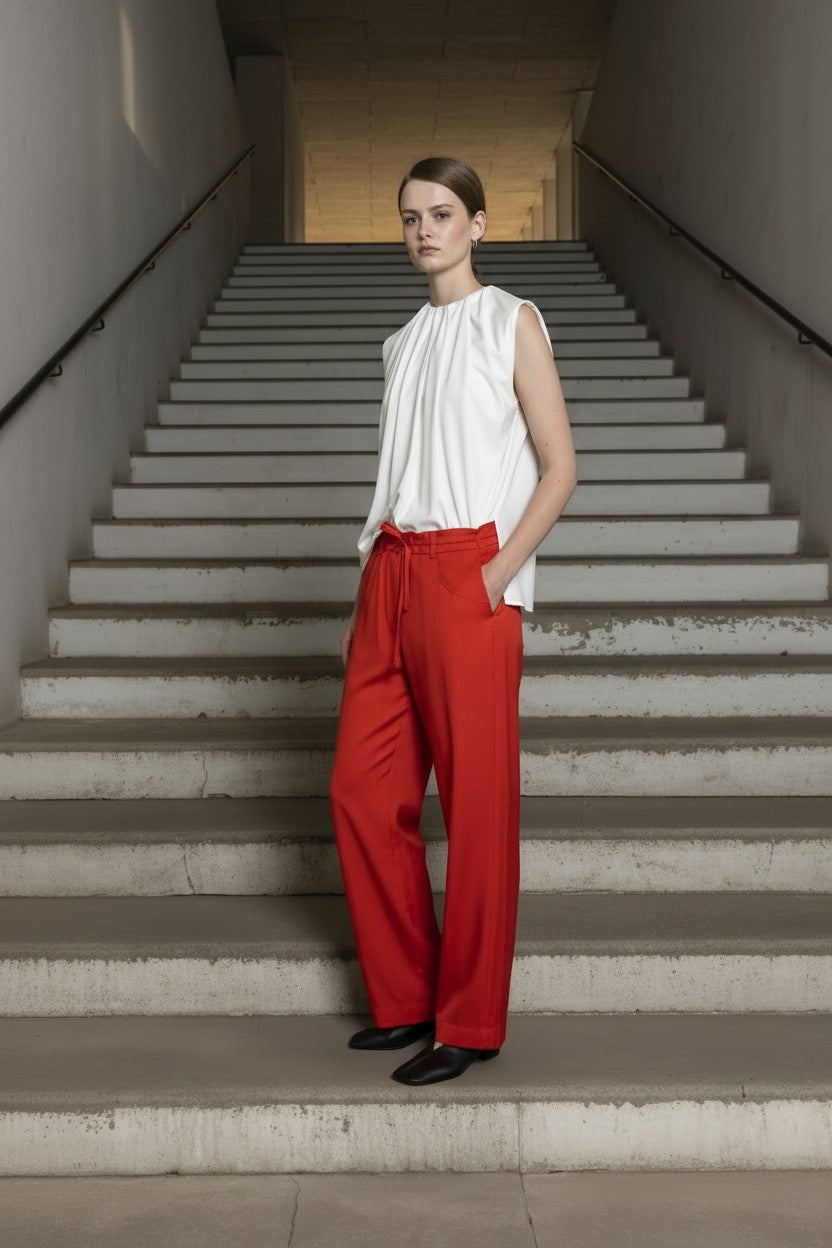Woman in a white sleeveless top and red pants standing on a staircase.