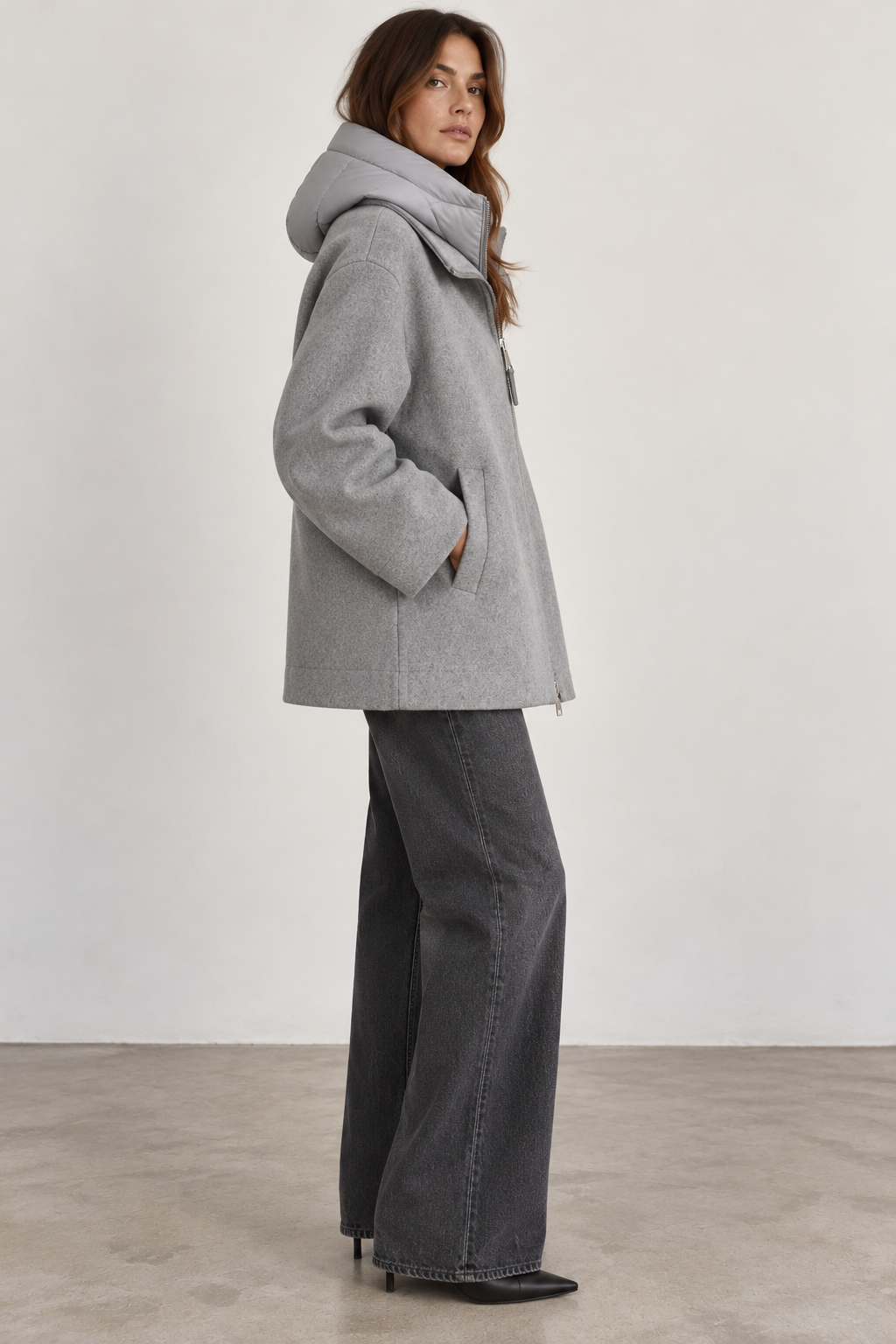 Side view of model wearing a Seventy gray wool-blend coat featuring a relaxed, boxy silhouette, removable padded collar, long sleeves, and discreet side pockets, paired with charcoal wide-leg jeans and black pointed-toe boots.