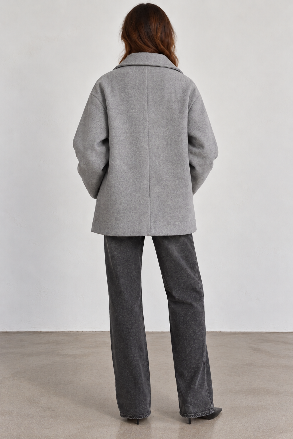 Back view of model wearing a Seventy gray wool-blend coat without the removable padded collar, featuring a relaxed, boxy silhouette, classic fold-down collar, dropped shoulders, long sleeves, center-back seam, and straight hem, styled with charcoal wide-leg jeans and black pointed-toe boots.
