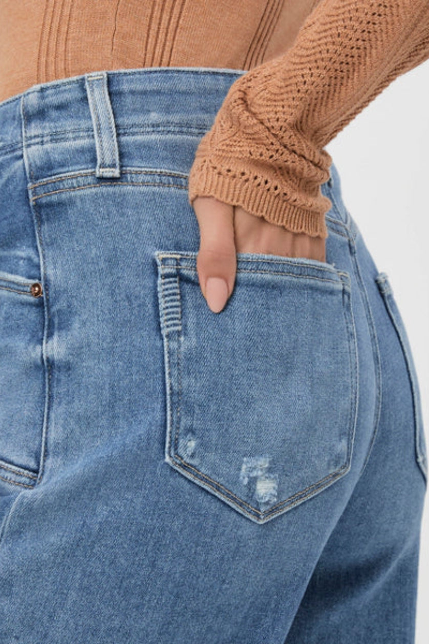 Close-up of blue jeans with a hand in the pocket against a white background.