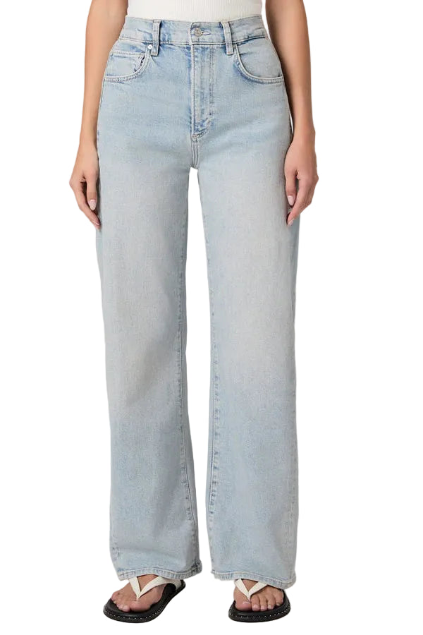 The bottom half of a woman wearing light wash barrel leg jeans and white and black flip flops on a plain background.