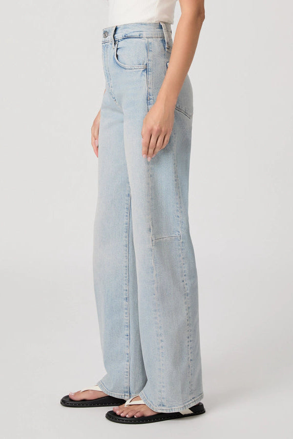 Side view of the bottom half of a woman wearing light wash barrel leg jeans with flip flops.