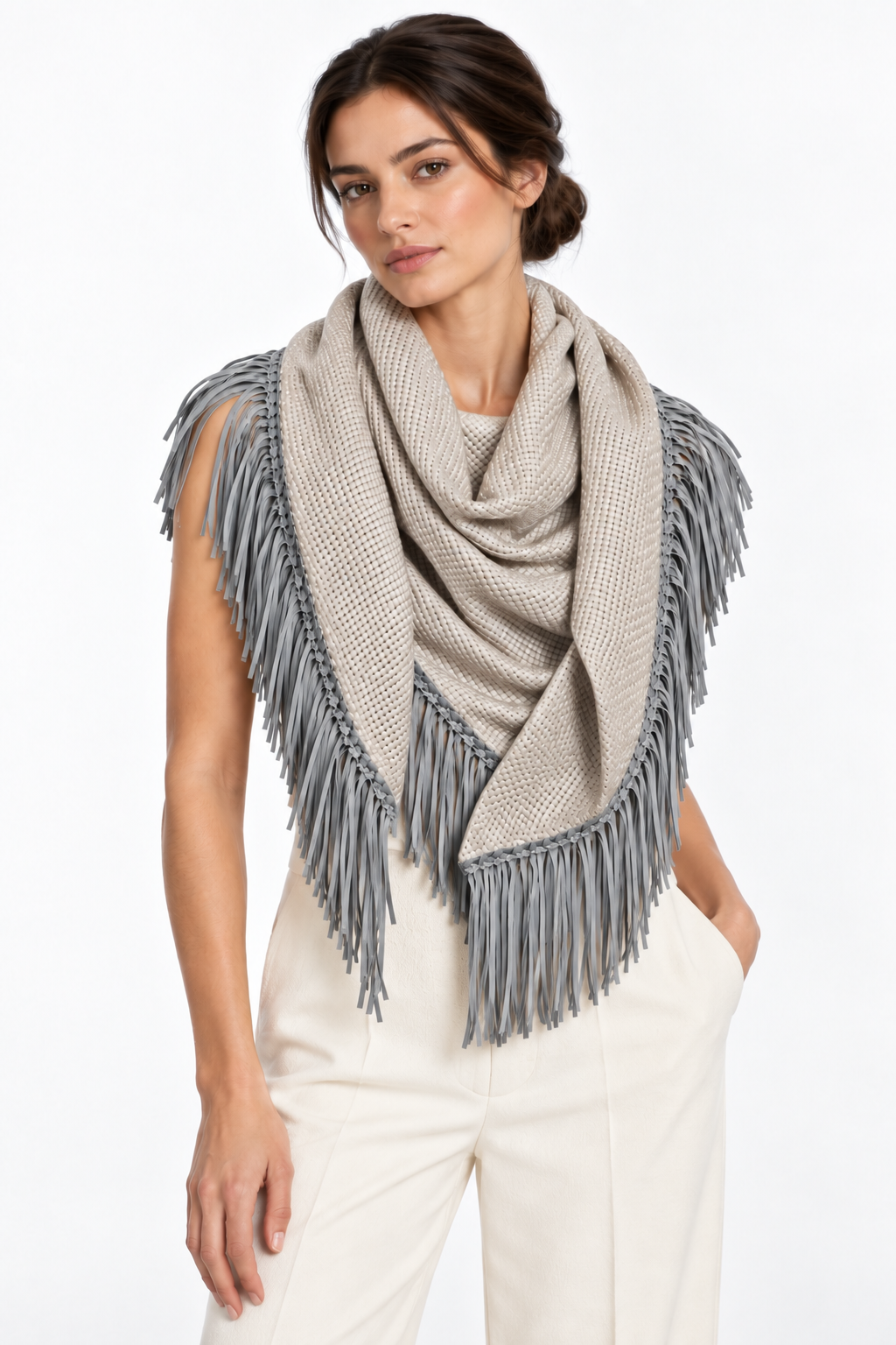Model wearing a taupe woven triangular scarf with cool gray fringe, styled with ivory wide-leg pants on a white background.