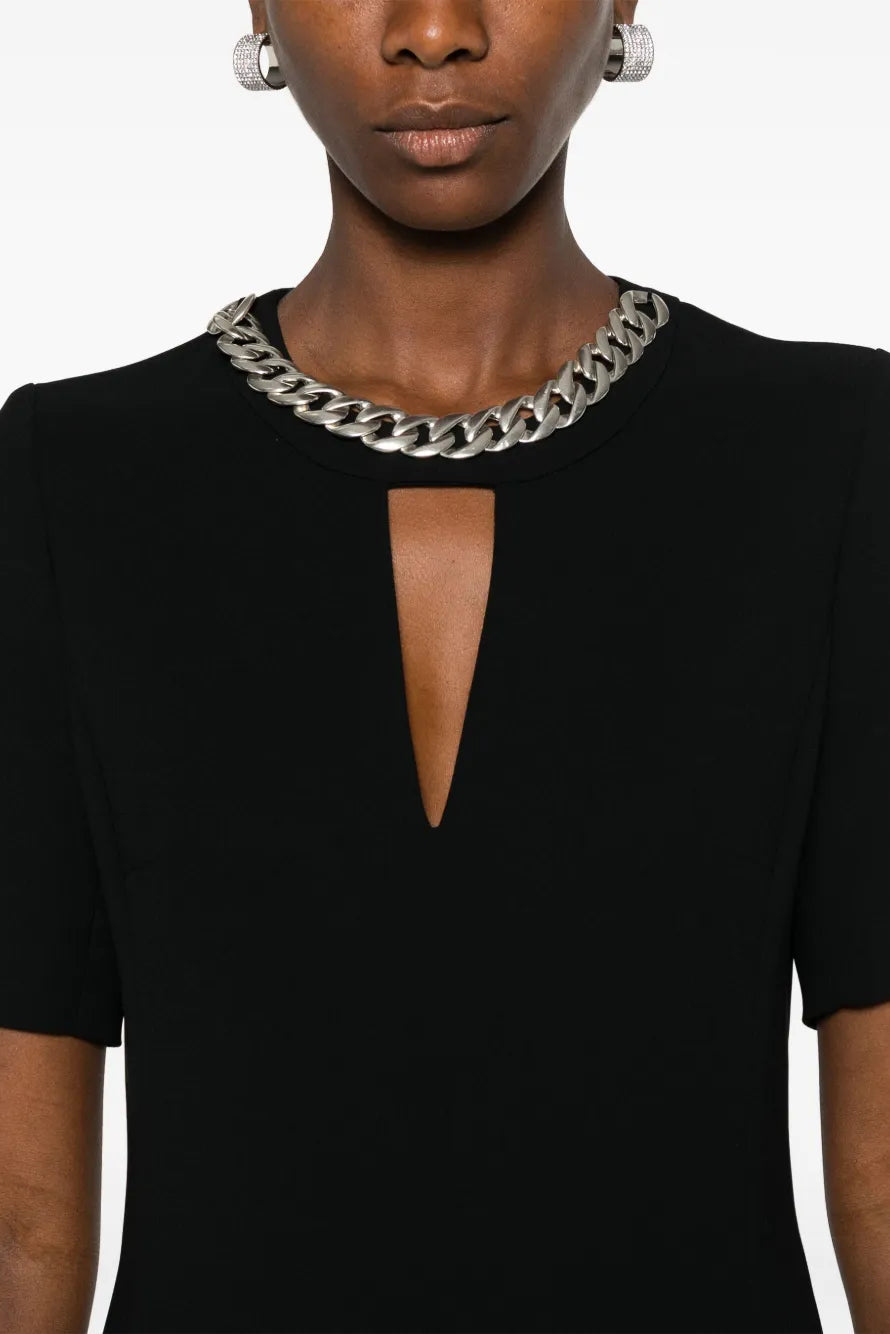 Woman wearing a black dress with a chain necklace on a white background.