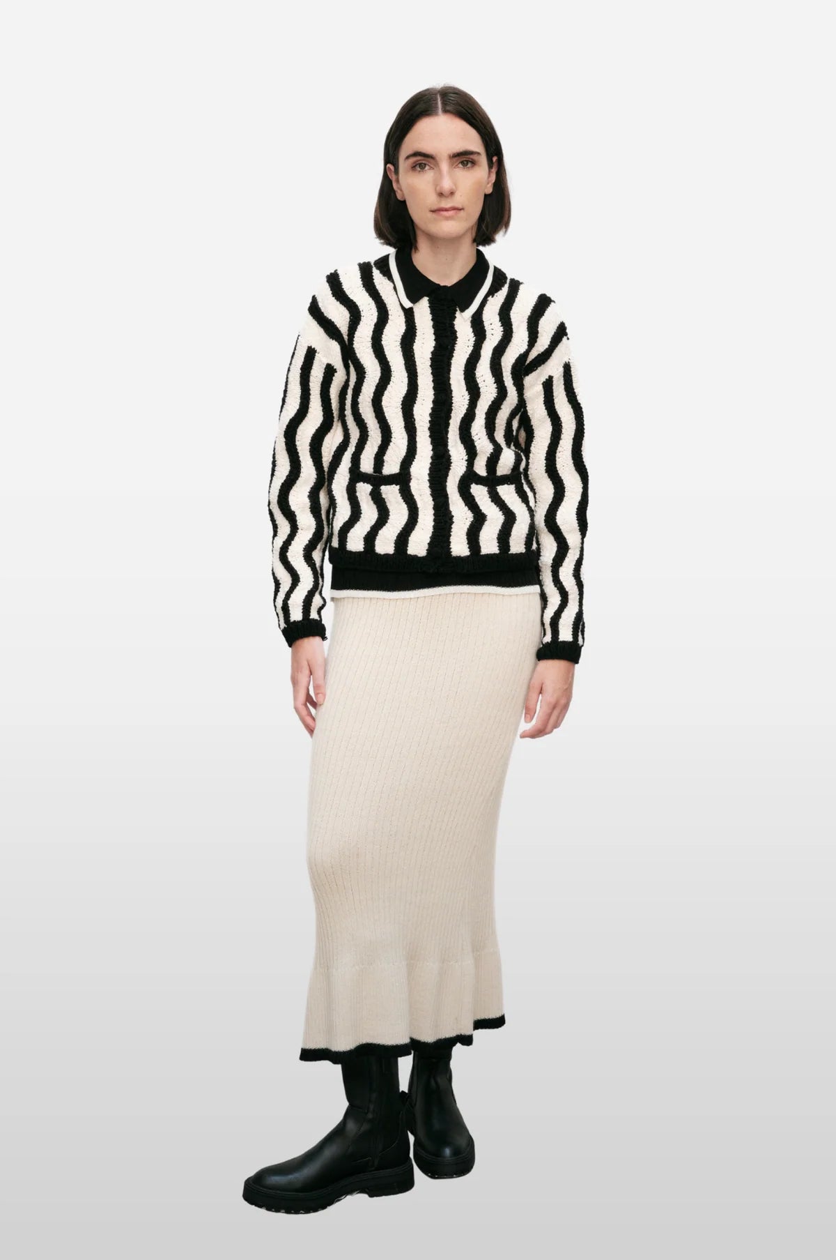 Woman wearing a black and white striped sweater with a long beige skirt on a white background.