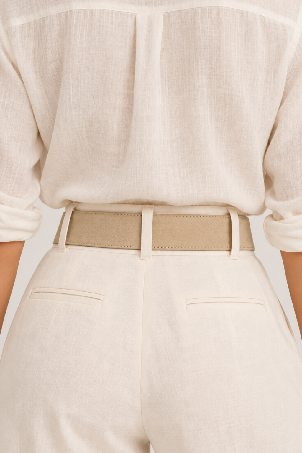Back view of a person wearing a cream linen shirt with rolled sleeves, a beige belt, and cream trousers.
