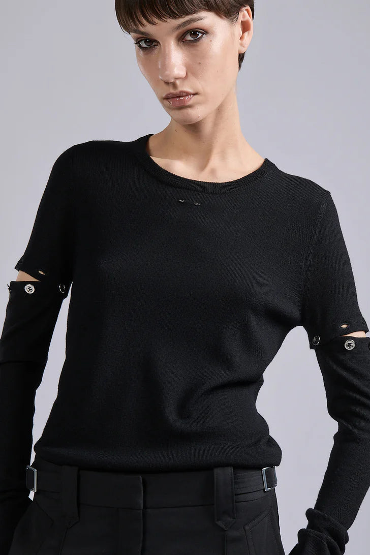 Woman wearing a black sweater with unique sleeve designs on a gray background
