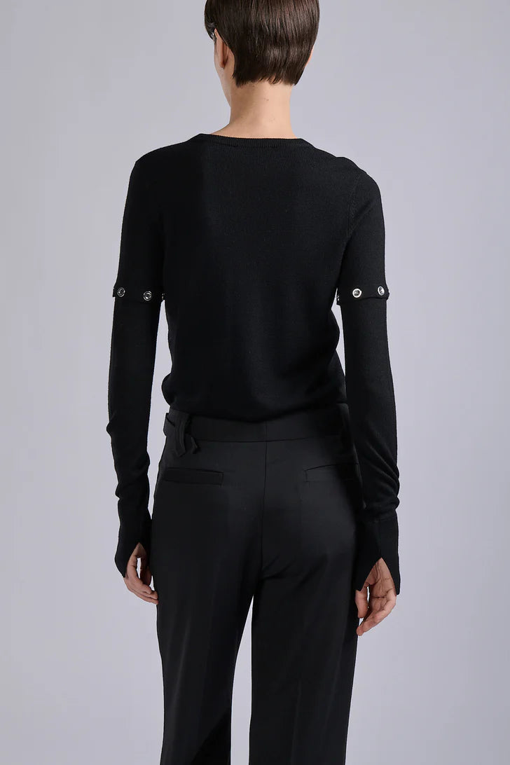 Person wearing a black long-sleeve top with decorative elements on a gray background