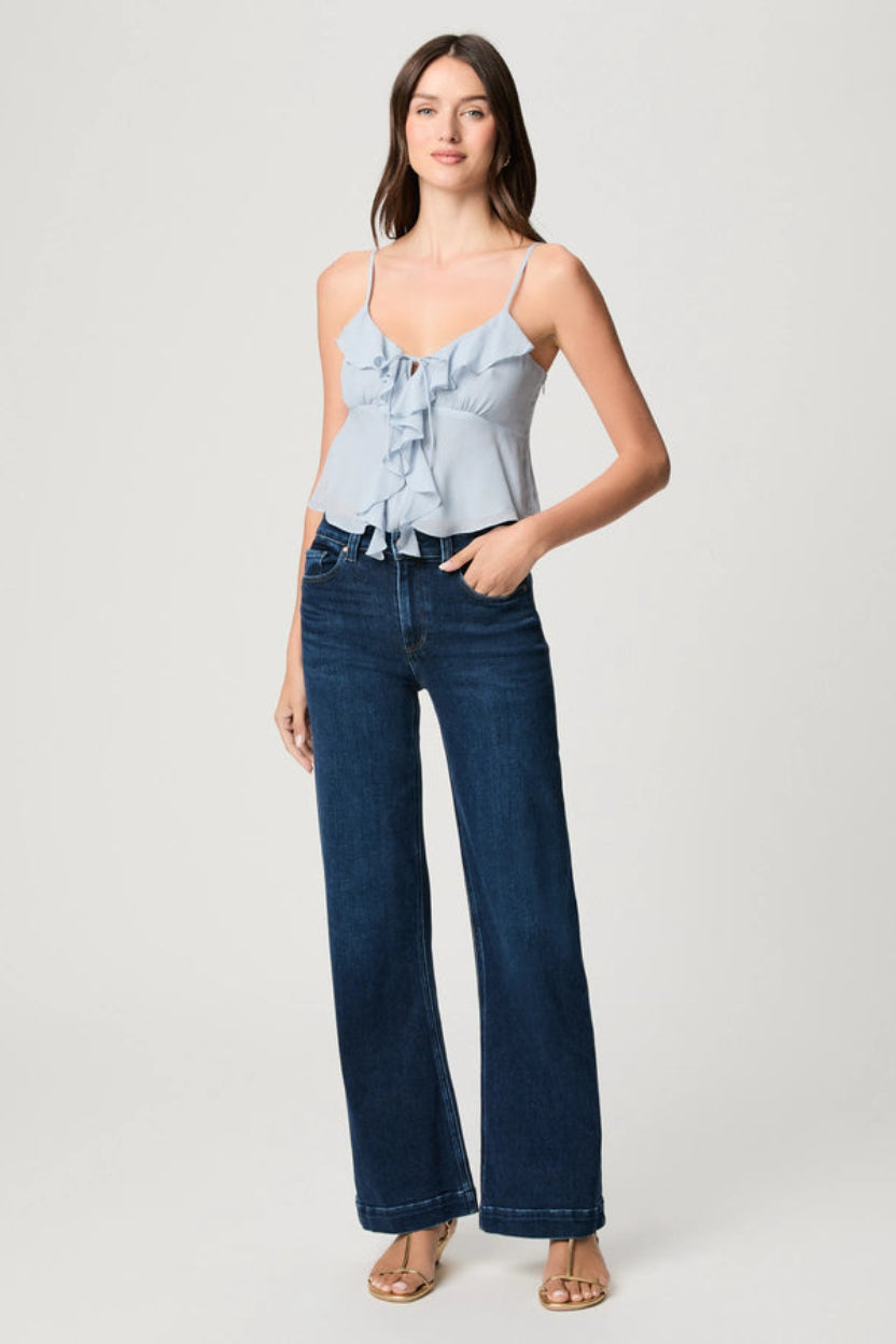 Woman wearing a light blue top and dark blue jeans on a white background.