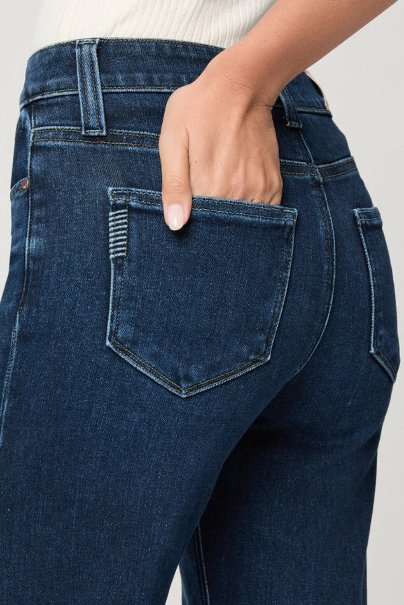 Close-up of blue jeans with a hand in the pocket against a neutral background.