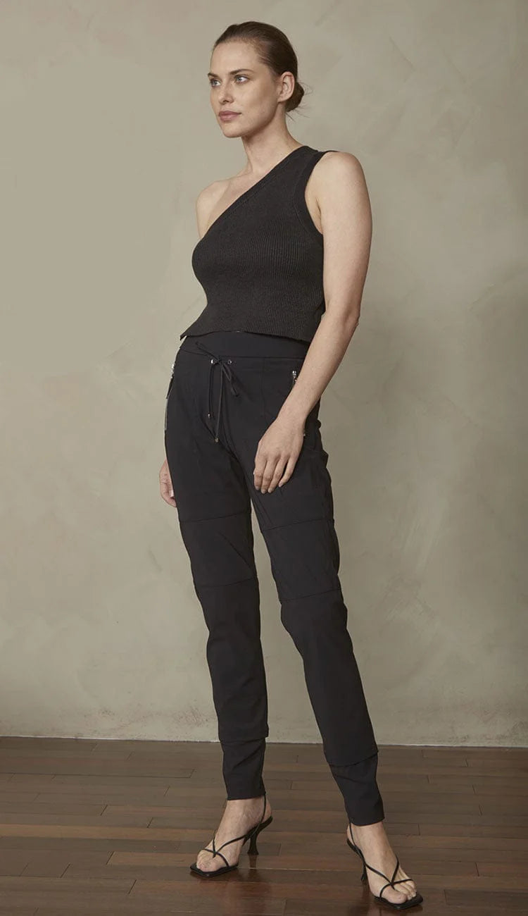 Woman wearing a black one-shoulder top and black drawstring pants against a plain background.