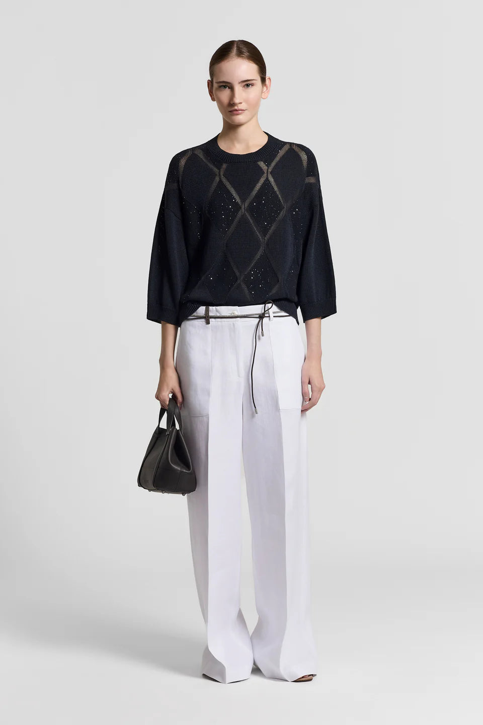 Woman wearing a dark blue sweater with geometric pattern and white pants on a light gray background