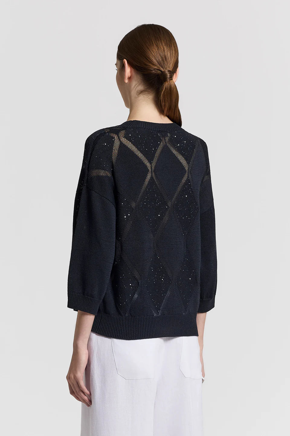 The back of a woman wearing a dark blue sweater with geometric pattern on a light gray background.