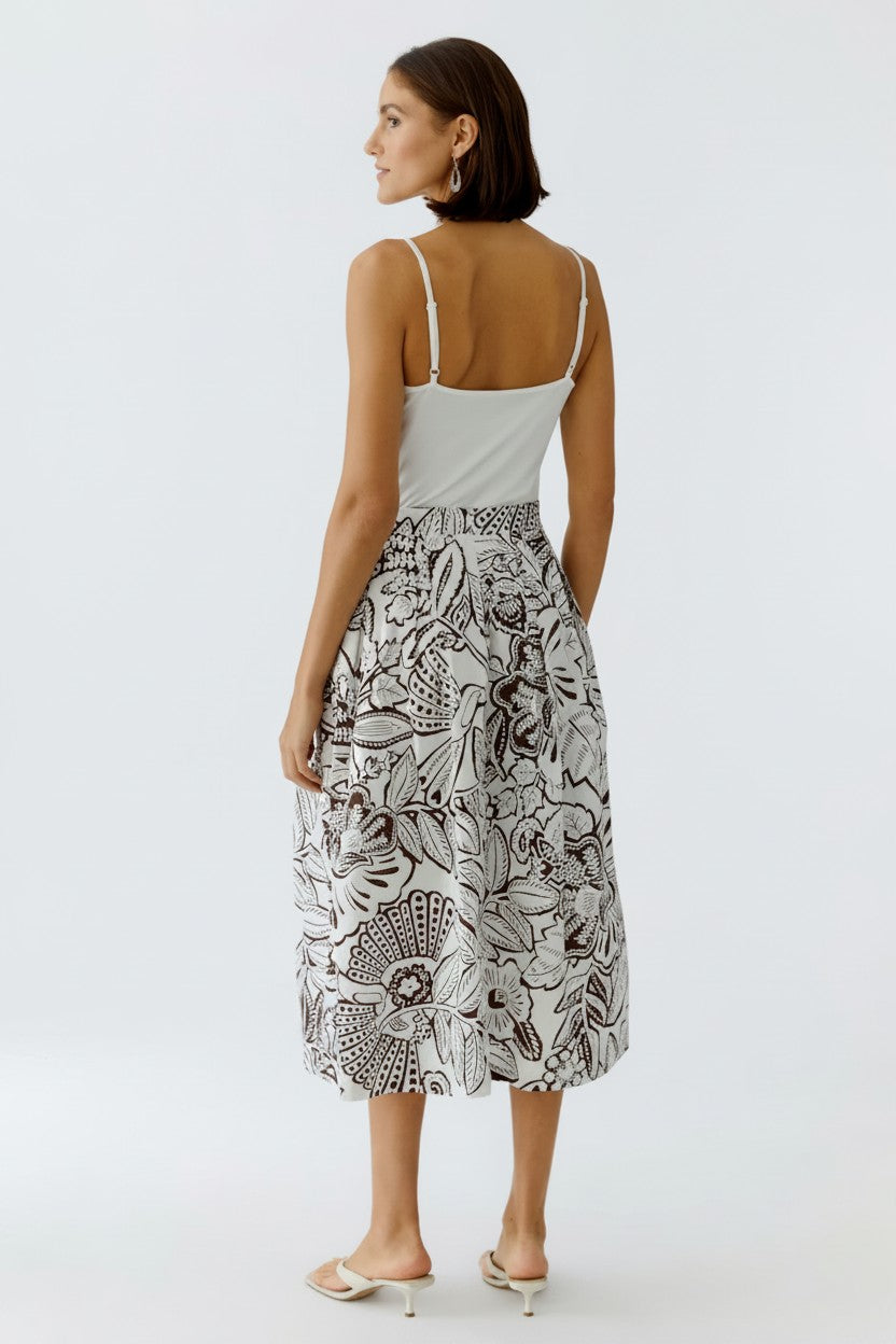 The back of a woman wearing a white top and patterned skirt on a white background.