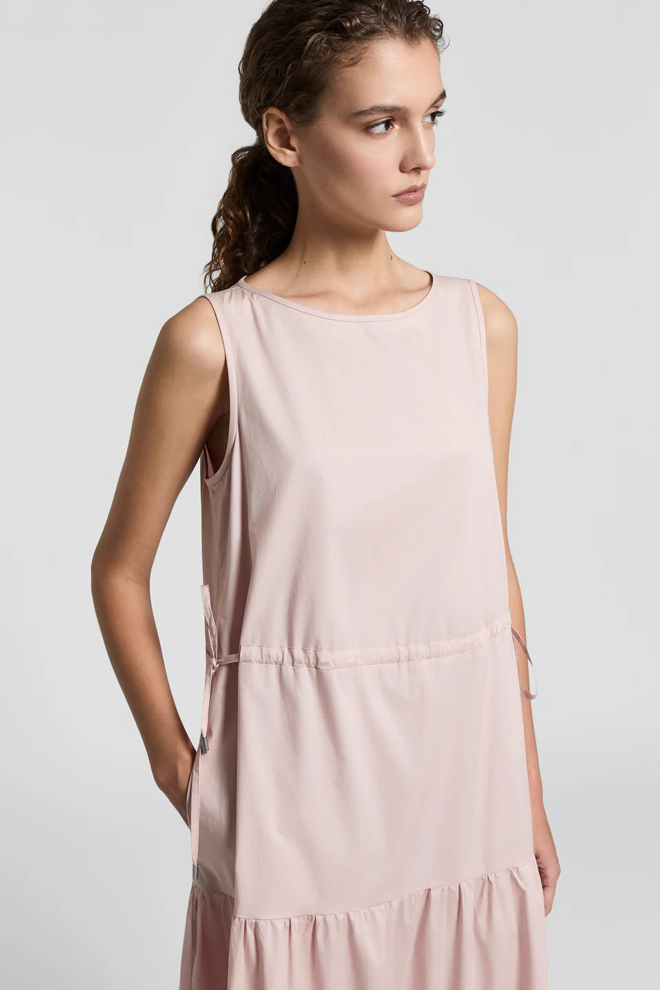 Close-up of a woman wearing a light pink sleeveless dress against a plain background.