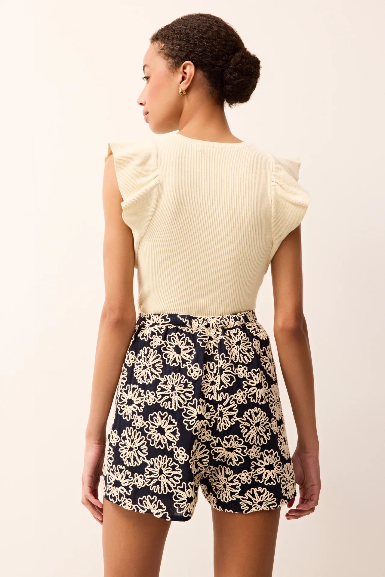 Woman wearing a cream top and navy floral shorts on a plain background.