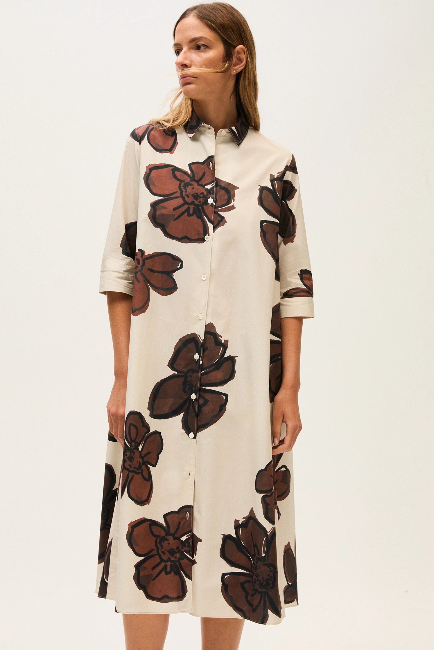 Woman wearing a cream-colored dress with large brown floral patterns on a white background.