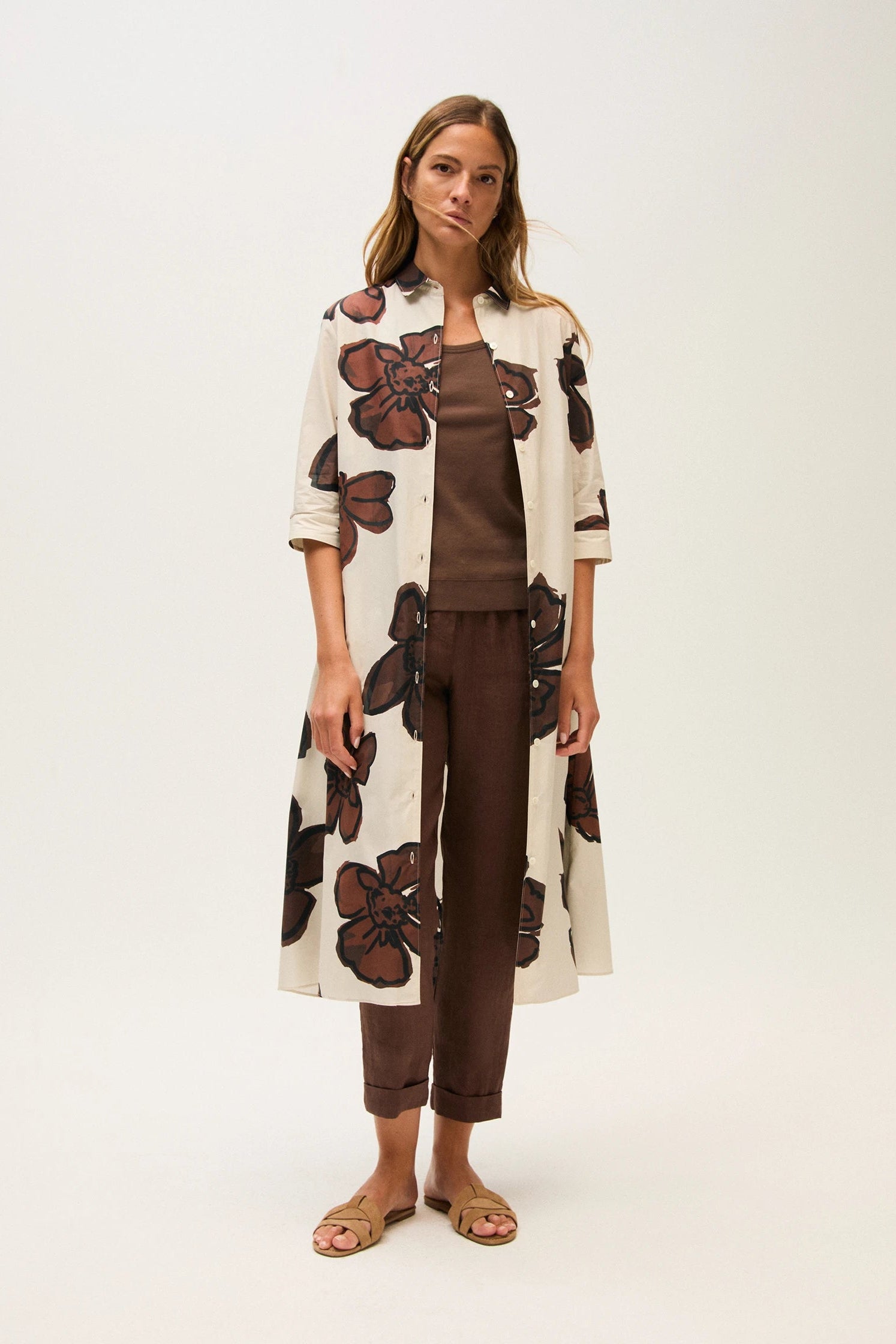 Woman wearing a floral pattern button dress over a brown outfit on a white background.
