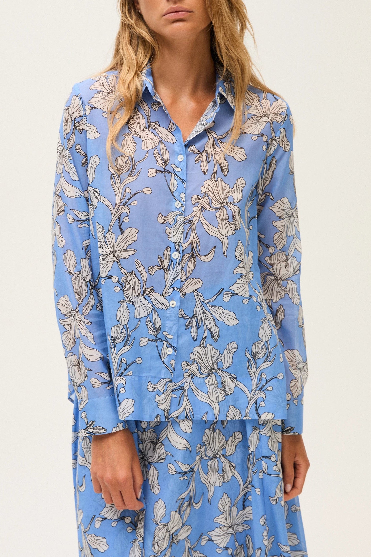 Close-up of a woman wearing a blue floral blouse and skirt against a light gray background.