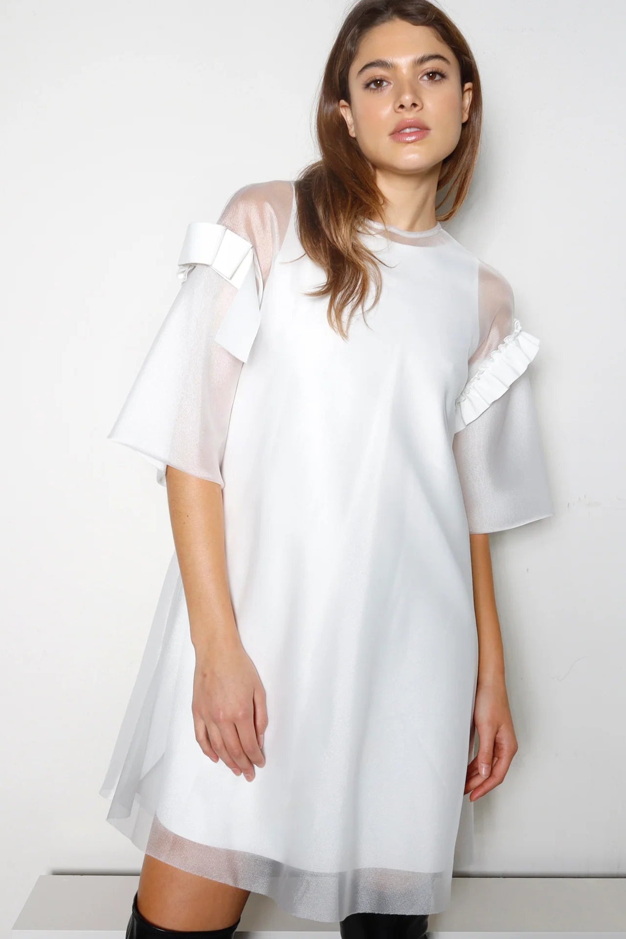 Woman wearing a white dress with sheer sleeves against a plain background.