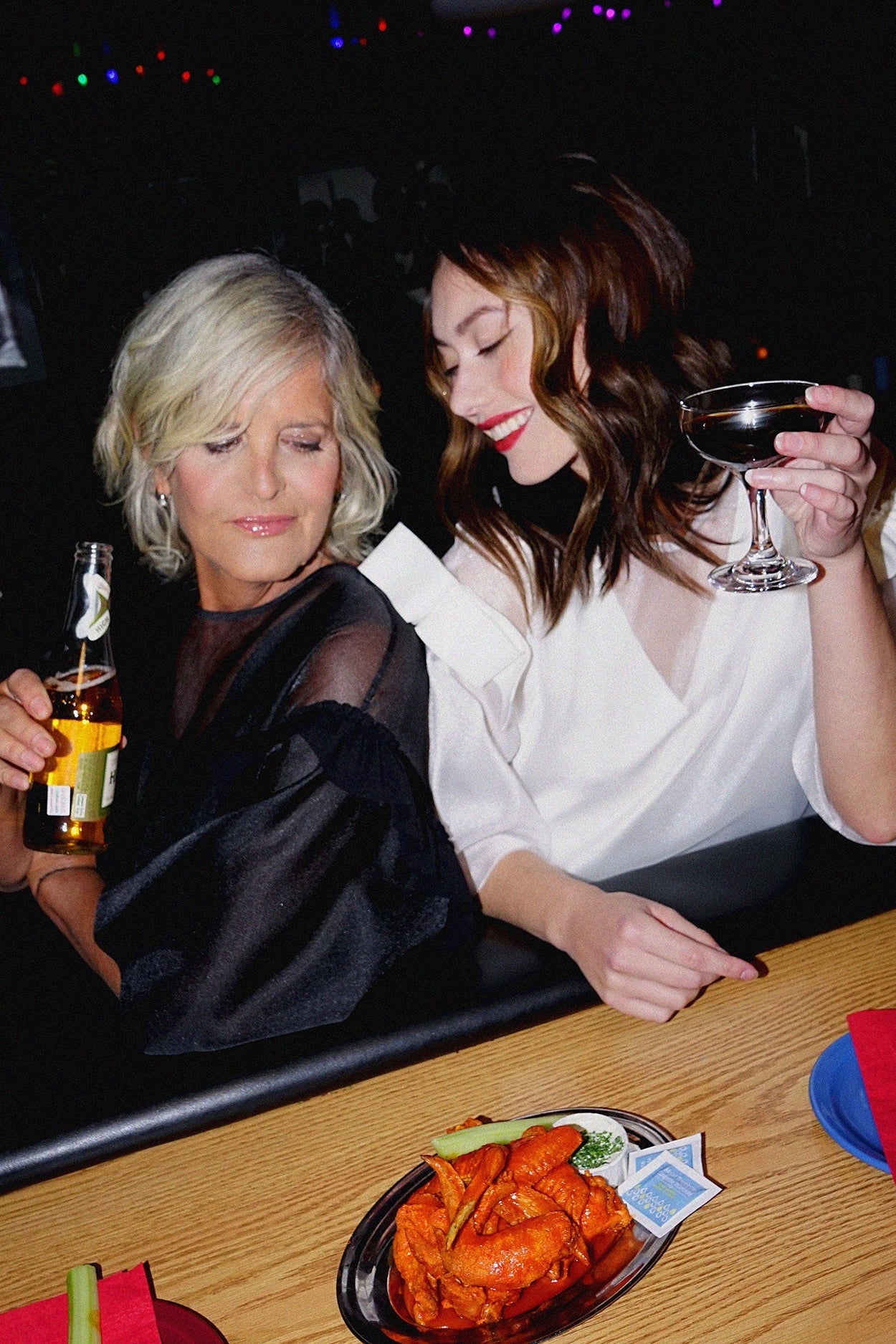 Two women sitting at a bar counter with drinks and food.