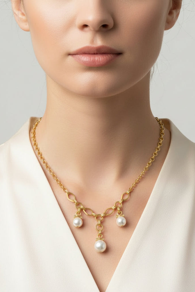 Gold necklace with pearl pendants worn by a person against a neutral background.