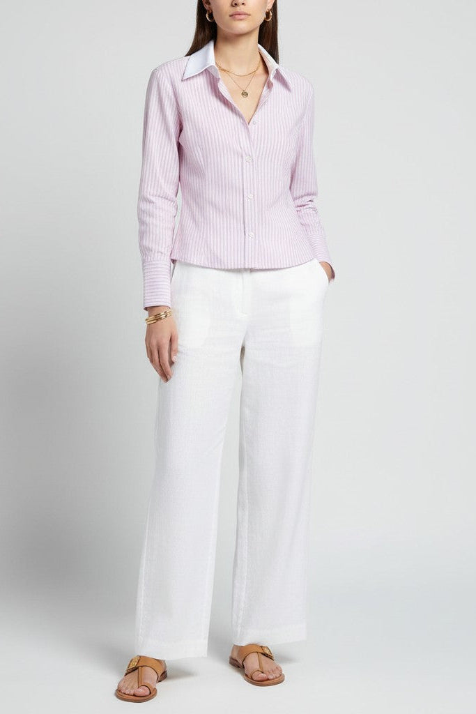 Close-up of a woman wearing a light pinkstriped shirt and white pants on a plain background.