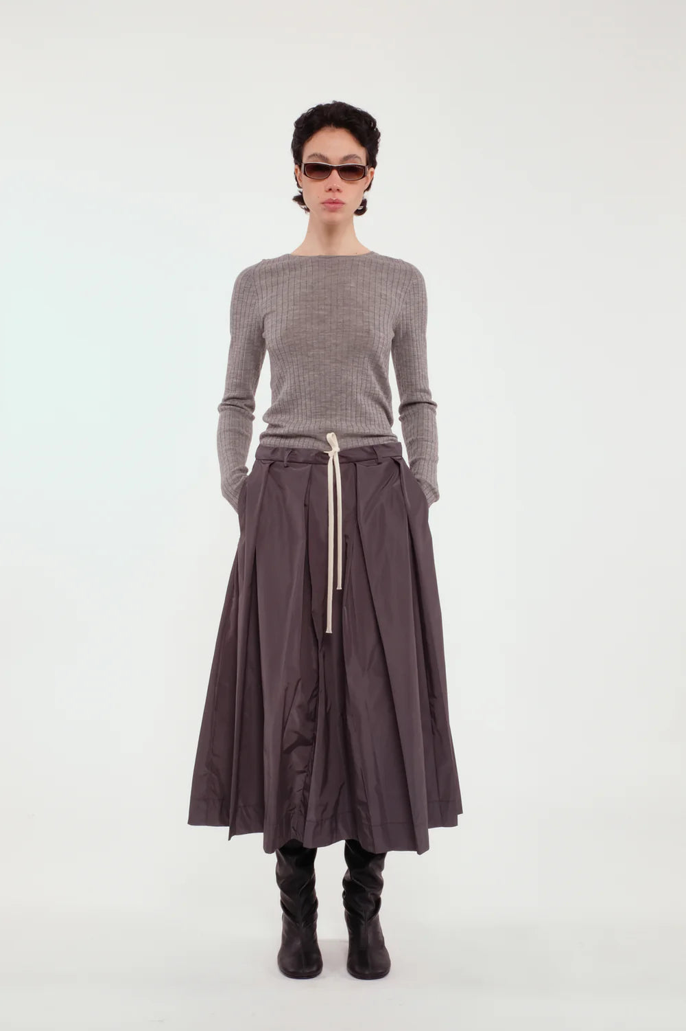 Person wearing a gray sweater and dark skirt on a white background.