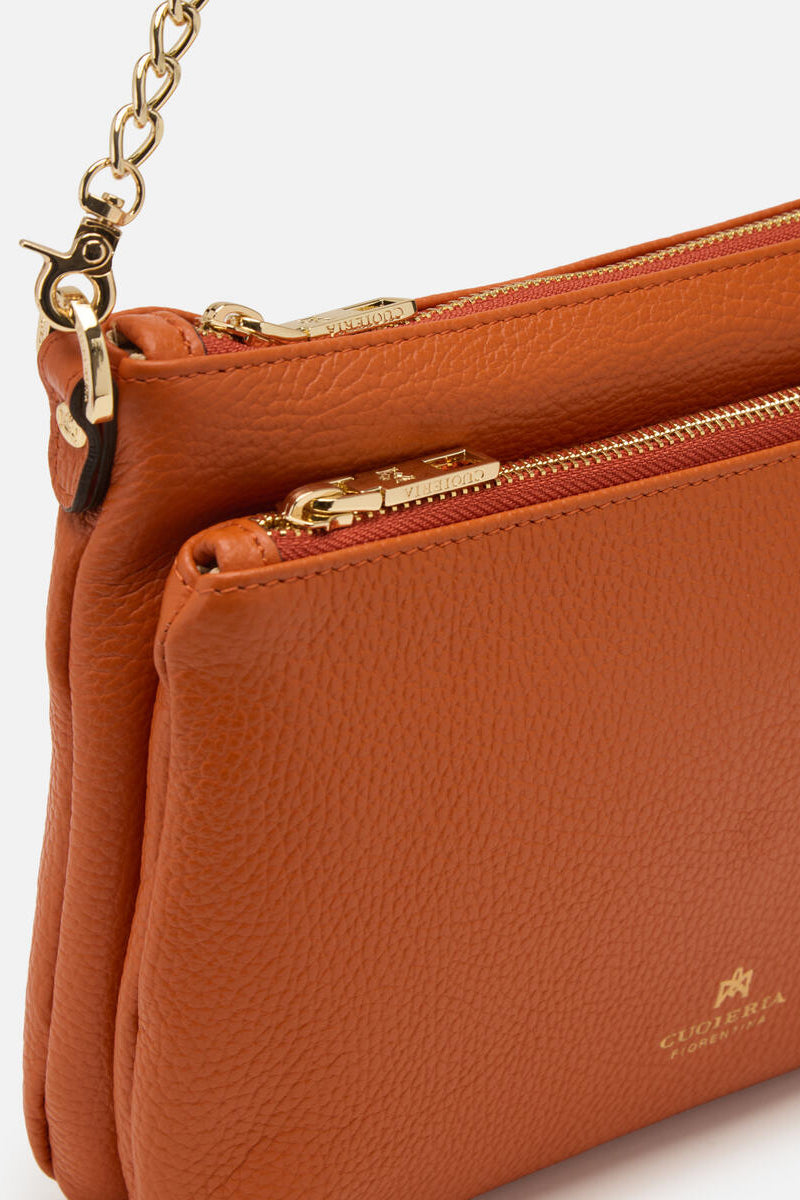 Orange leather handbag with gold zipper and chain detail on a light gray background.