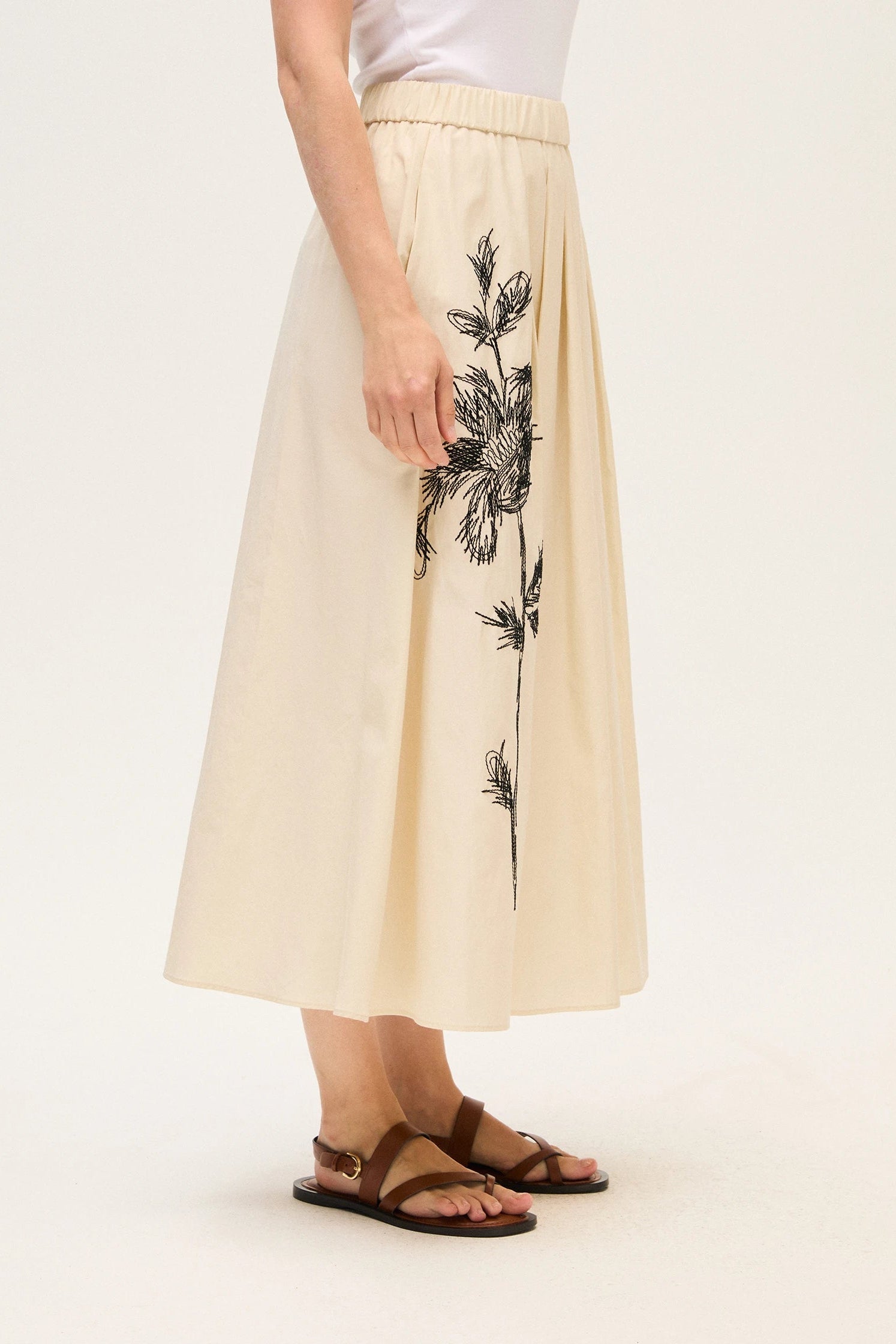 Beige skirt with black floral embroidery worn by a woman on a white background.