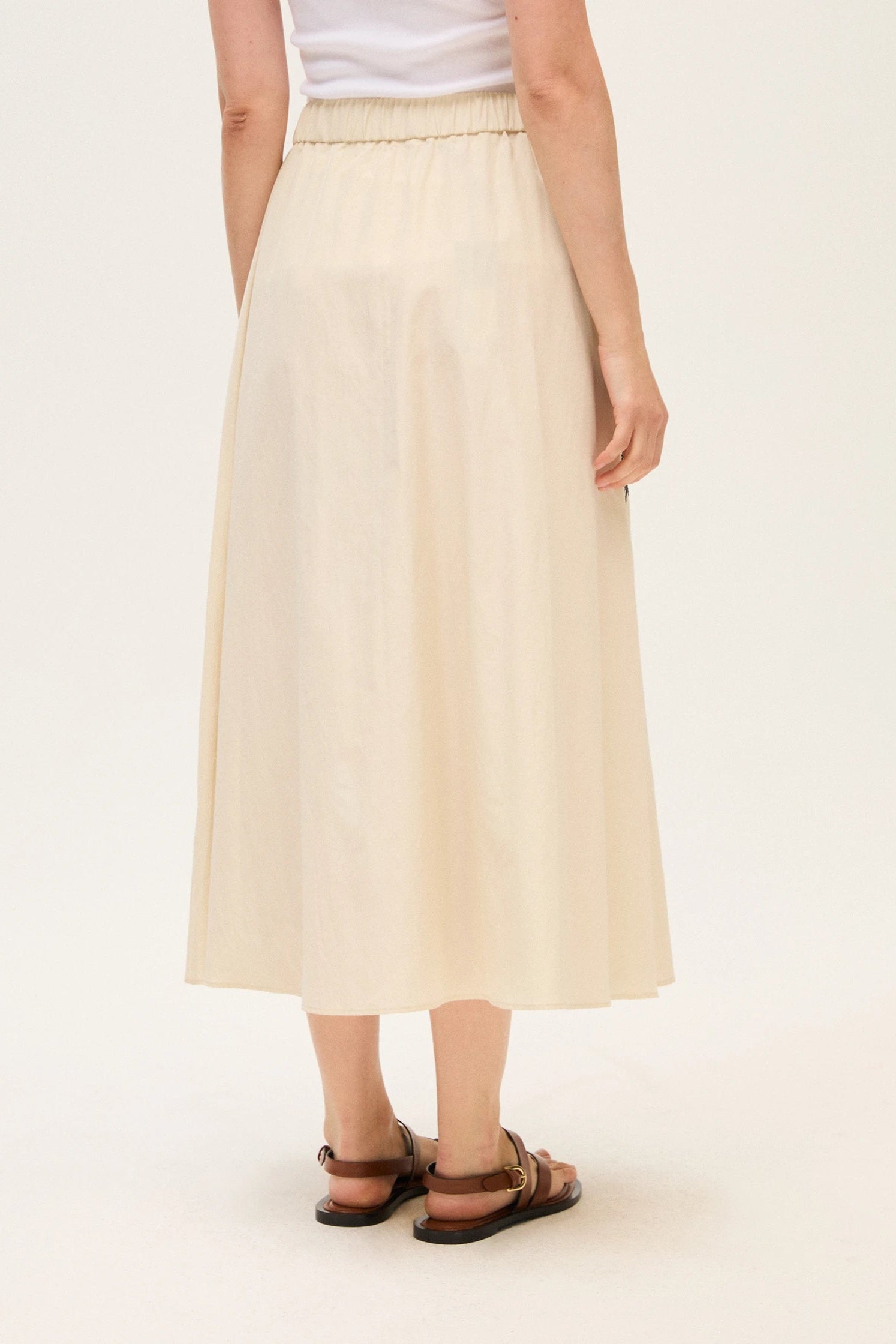 Back of a woman wearing a beige skirt on a white background.
