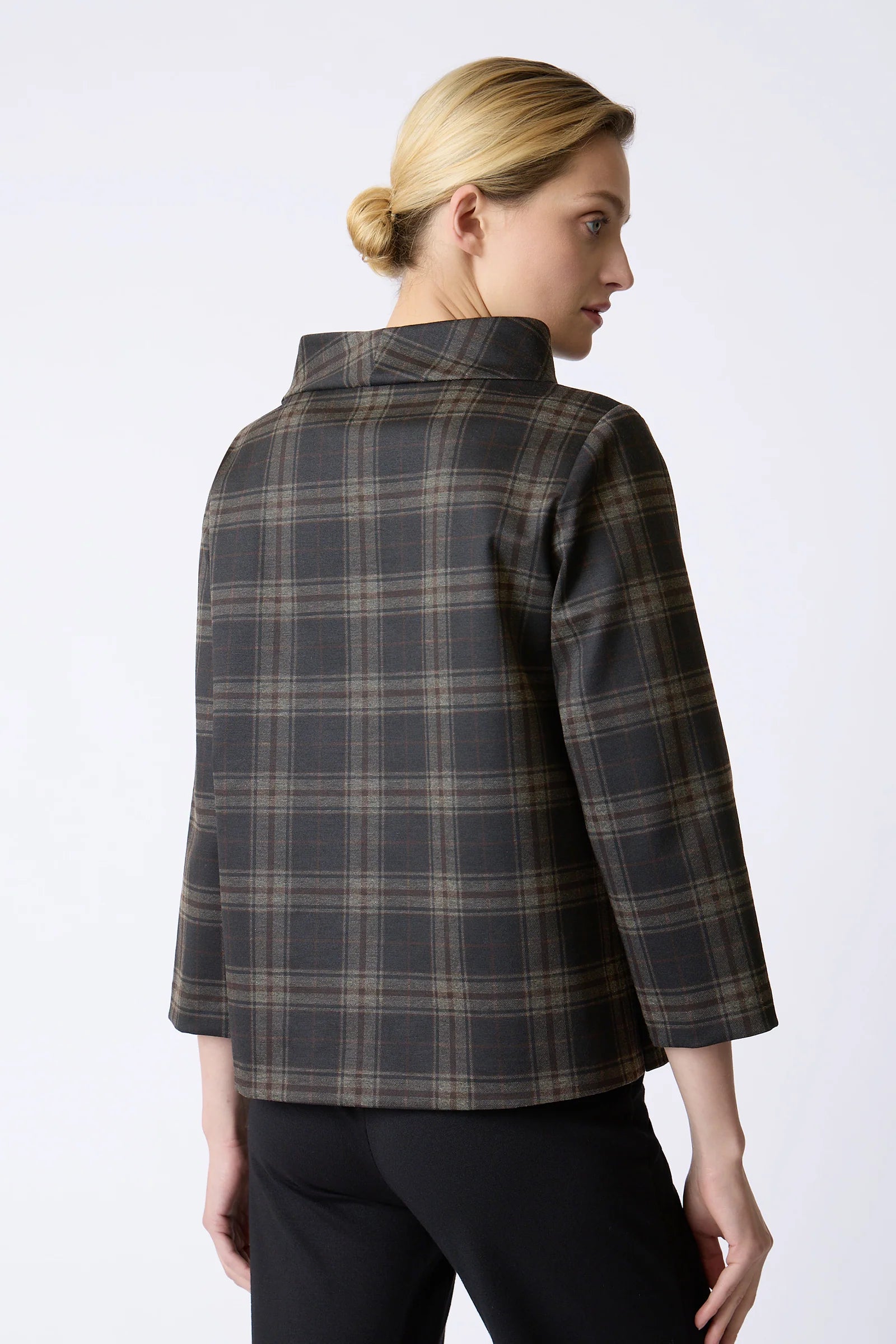 A woman shown from the back wearing a dark gray and black plaid jacket with beige lines, paired with black pants, against a light gray studio background.