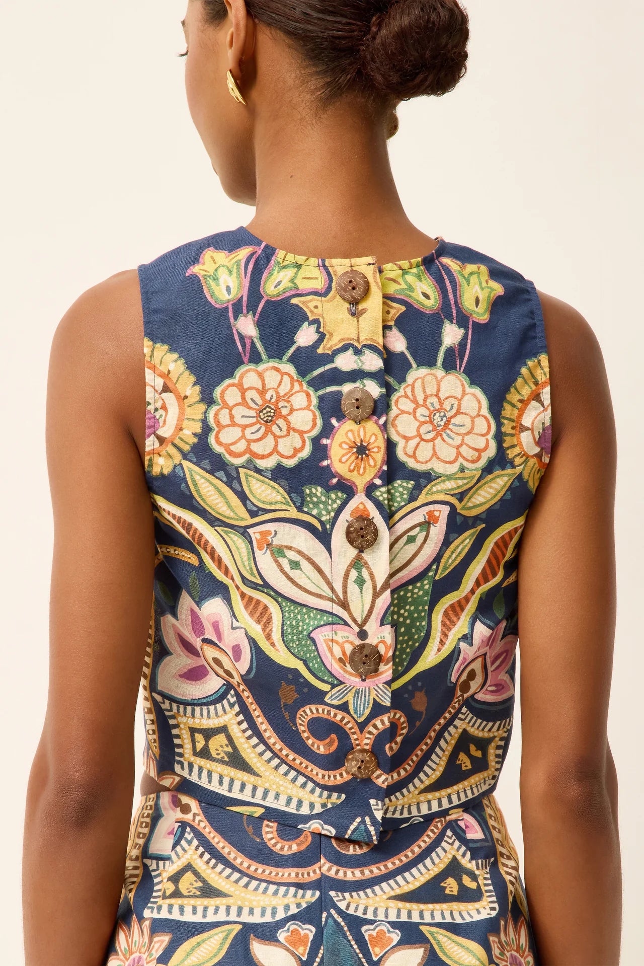 Woman wearing a sleeveless top with a colorful floral pattern on a plain background.