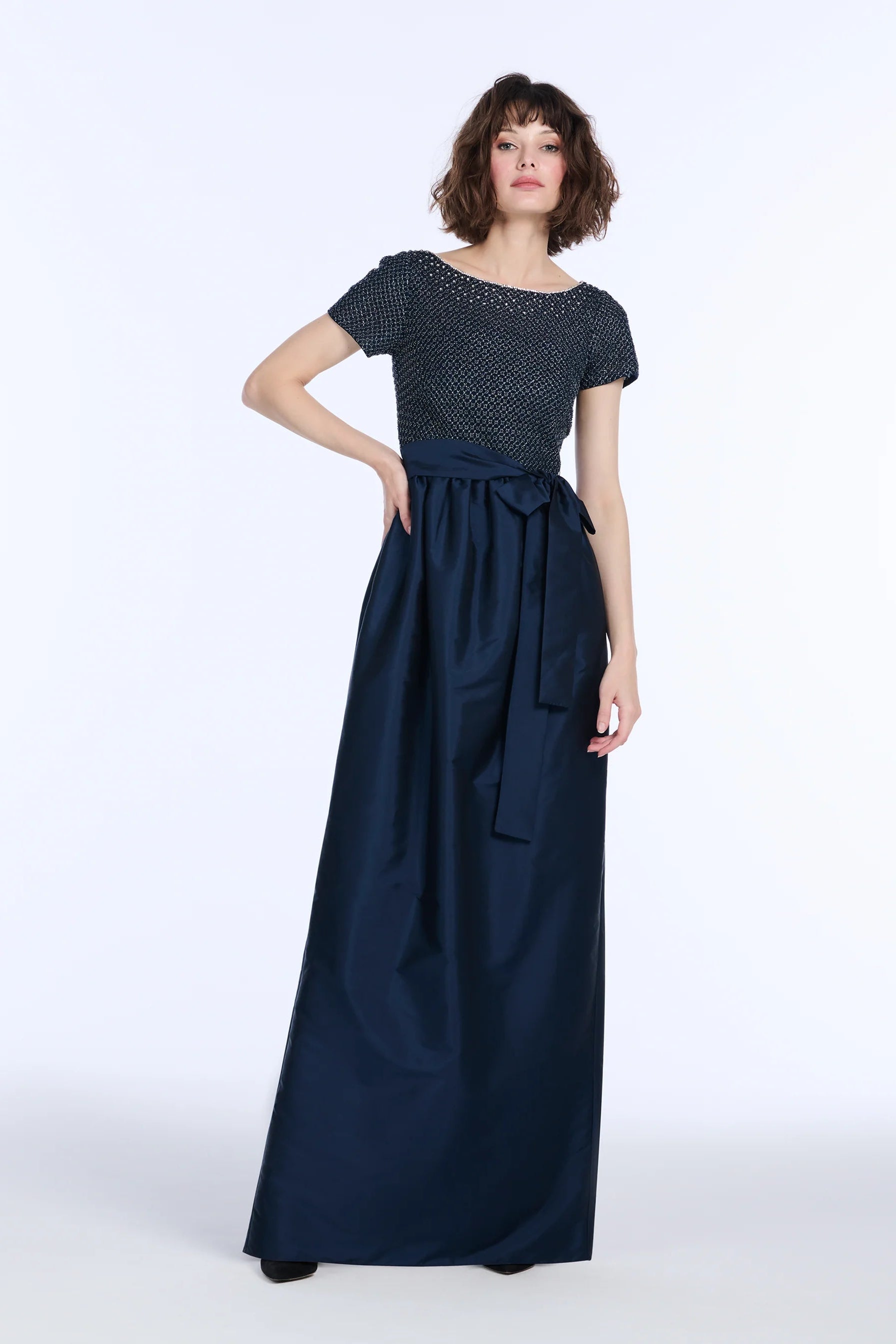 Woman wearing a long navy dress with a white background.