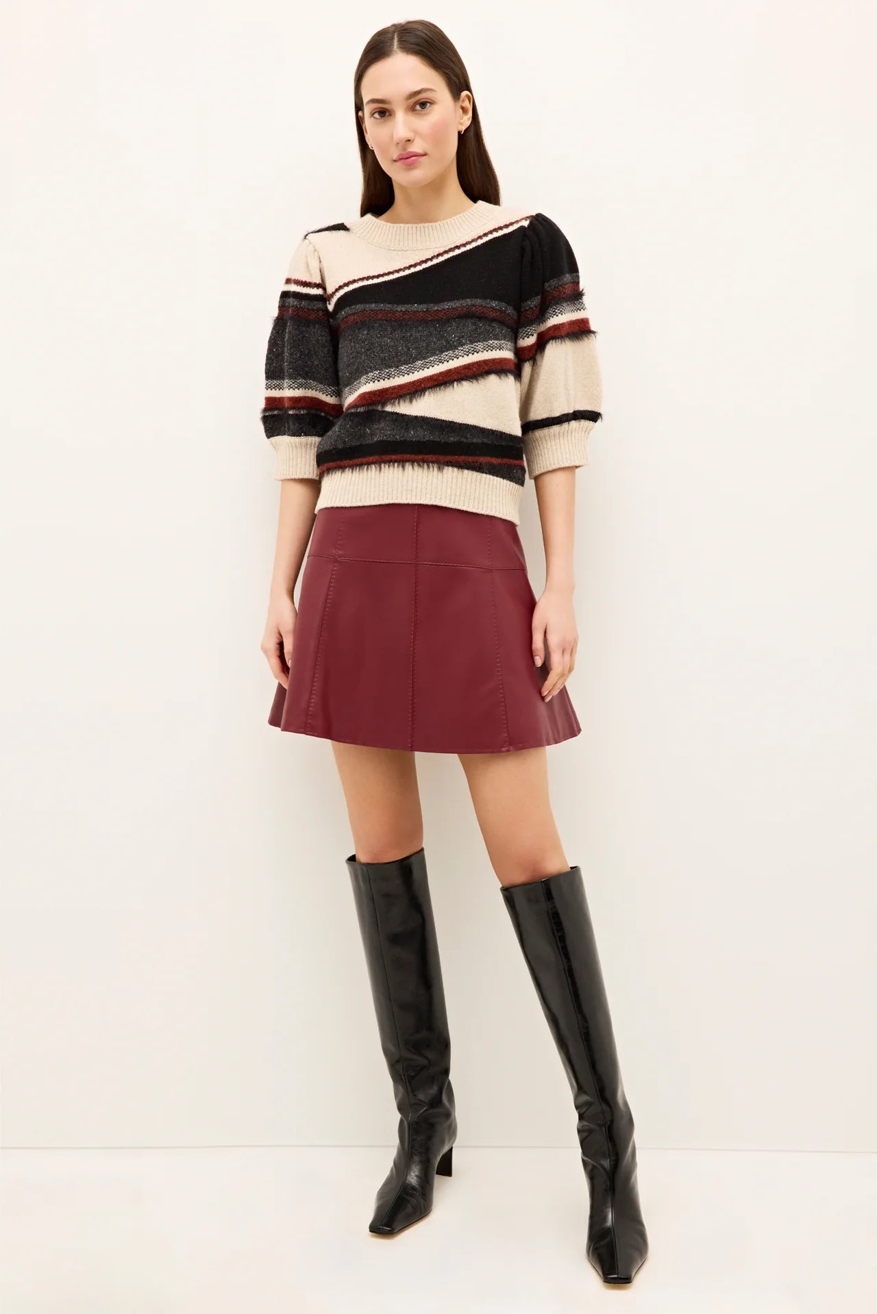Woman wearing a striped sweater, burgundy skirt, and black knee-high boots on a white background.
