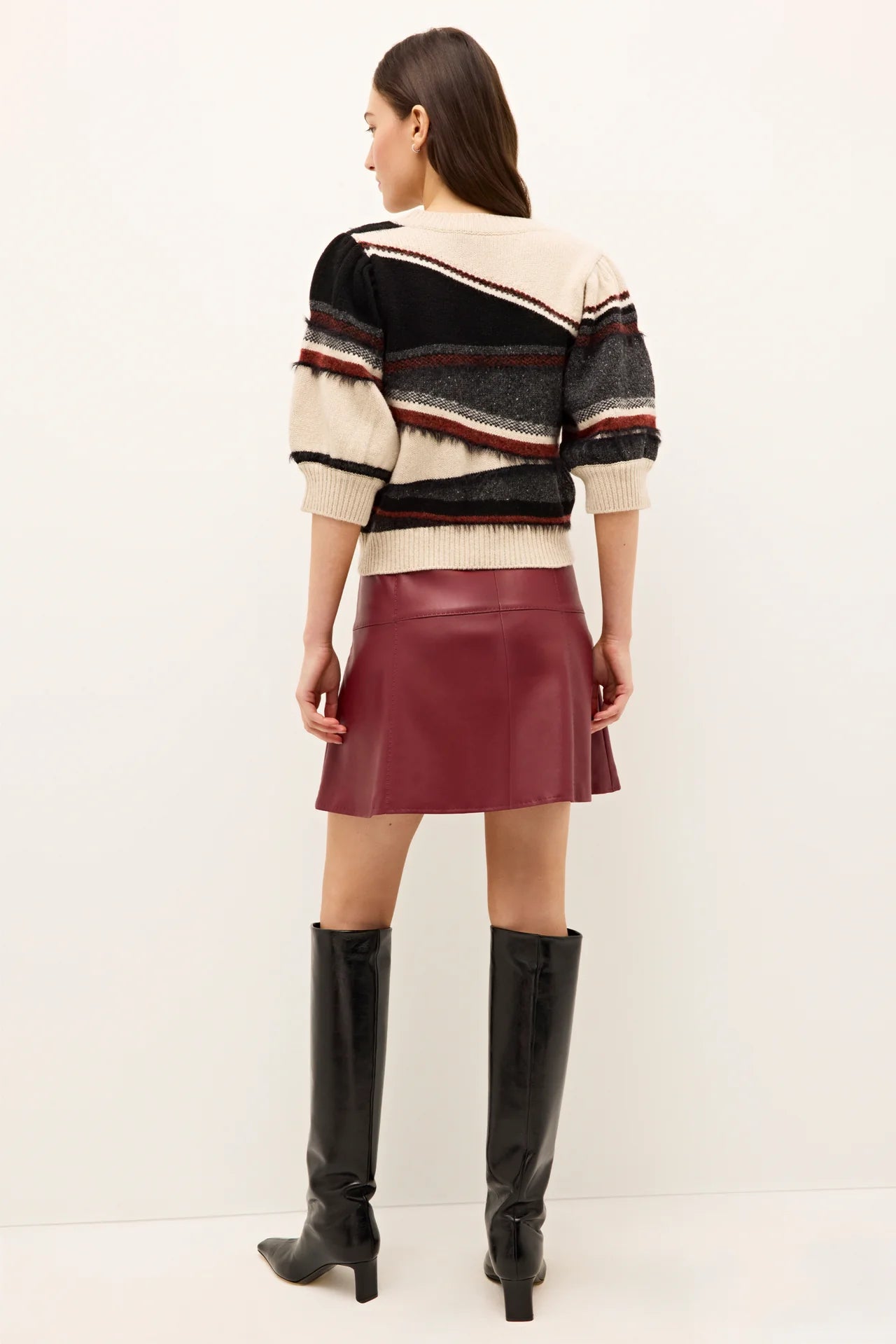 Woman wearing a striped sweater, red skirt, and black knee-high boots on a white background.