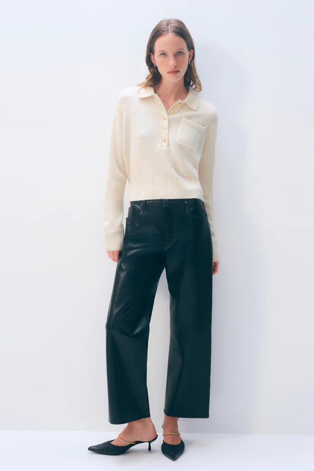 Woman wearing a cream blouse and dark pants against a white background.
