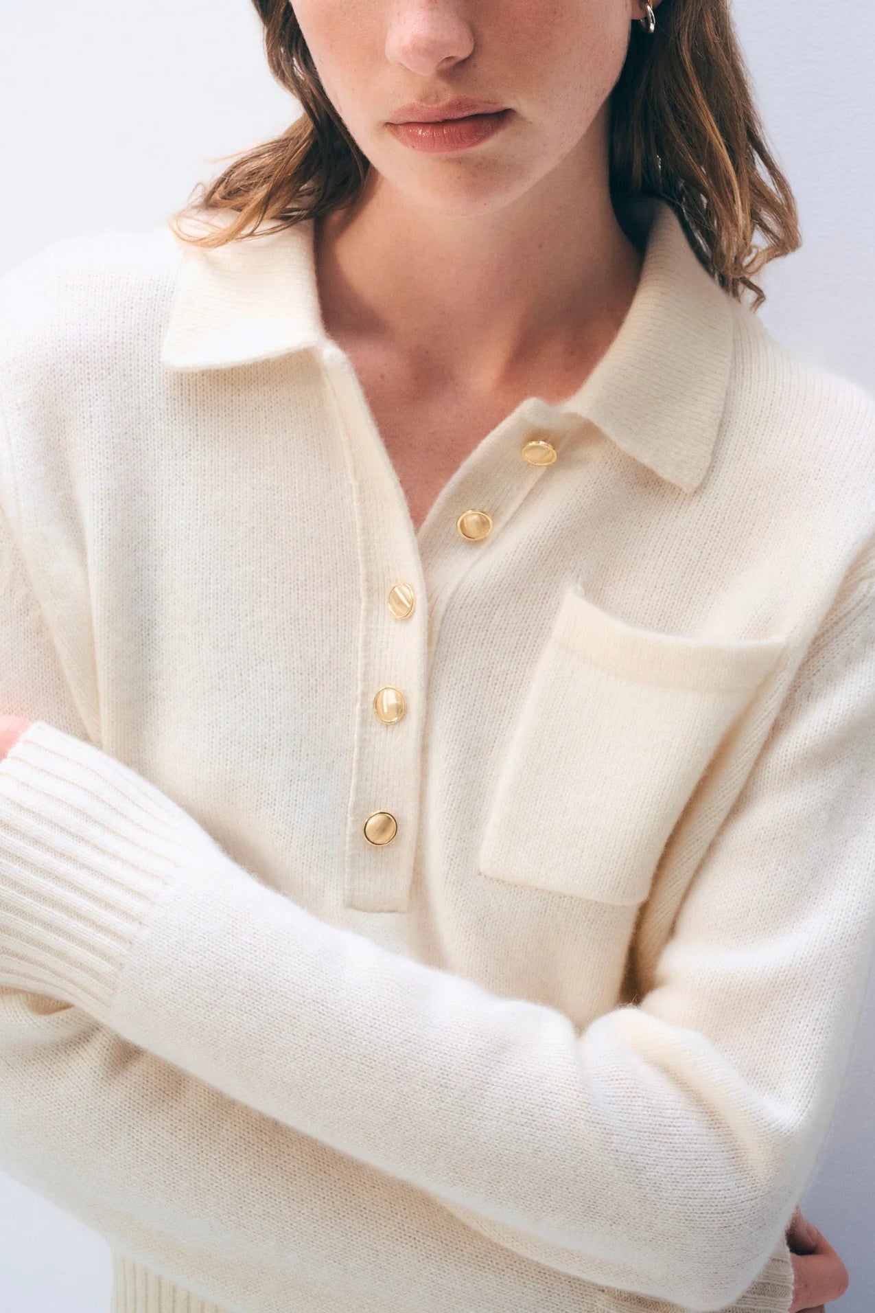 Close-up of a person wearing a cream-colored sweater with gold buttons on a white background.