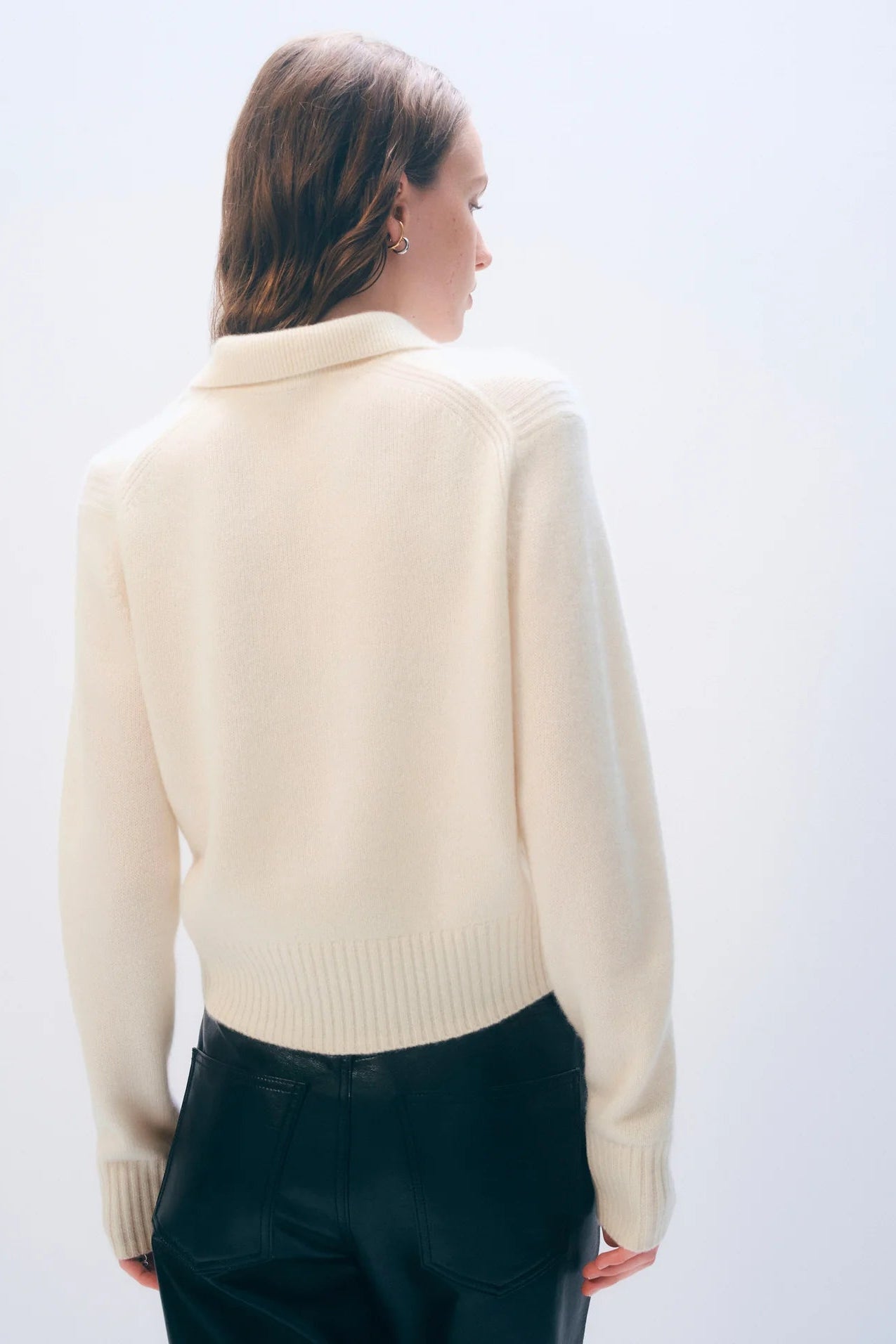 Woman wearing a cream sweater and dark pants against a white background.