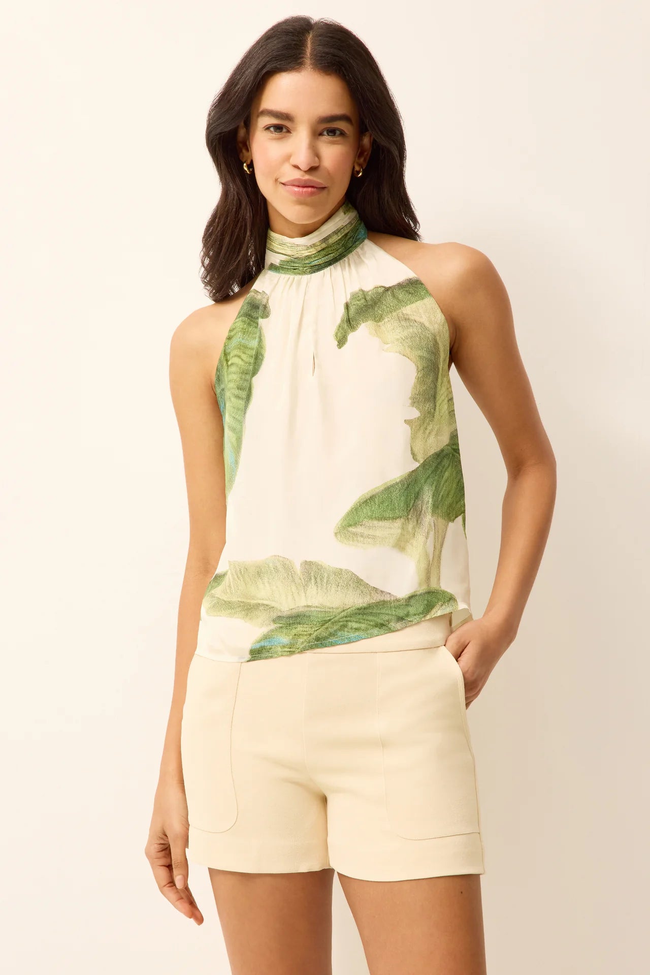 Woman wearing a green leaf-patterned top and beige shorts on a white background.