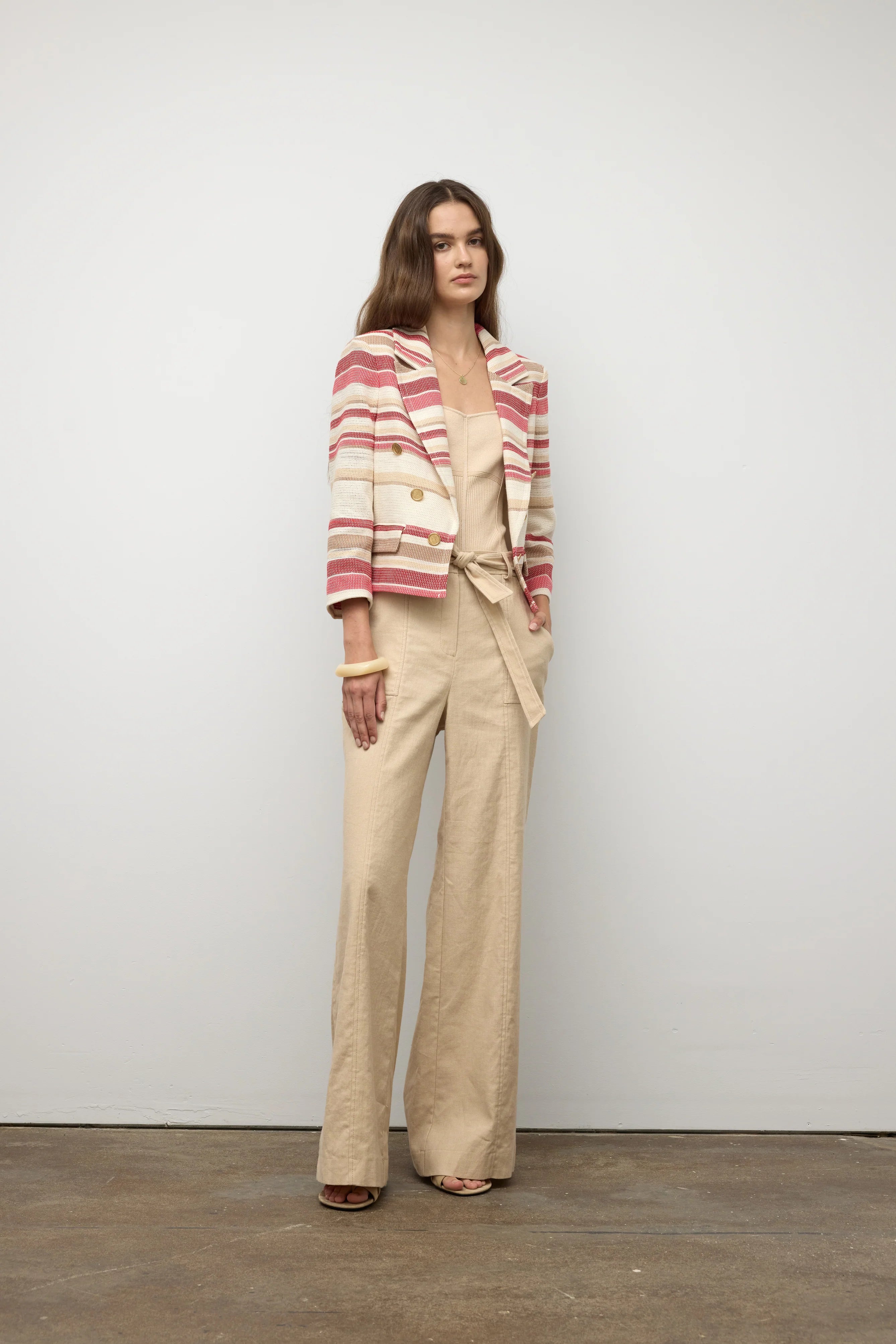 Woman wearing a striped blazer and beige pants against a plain background.