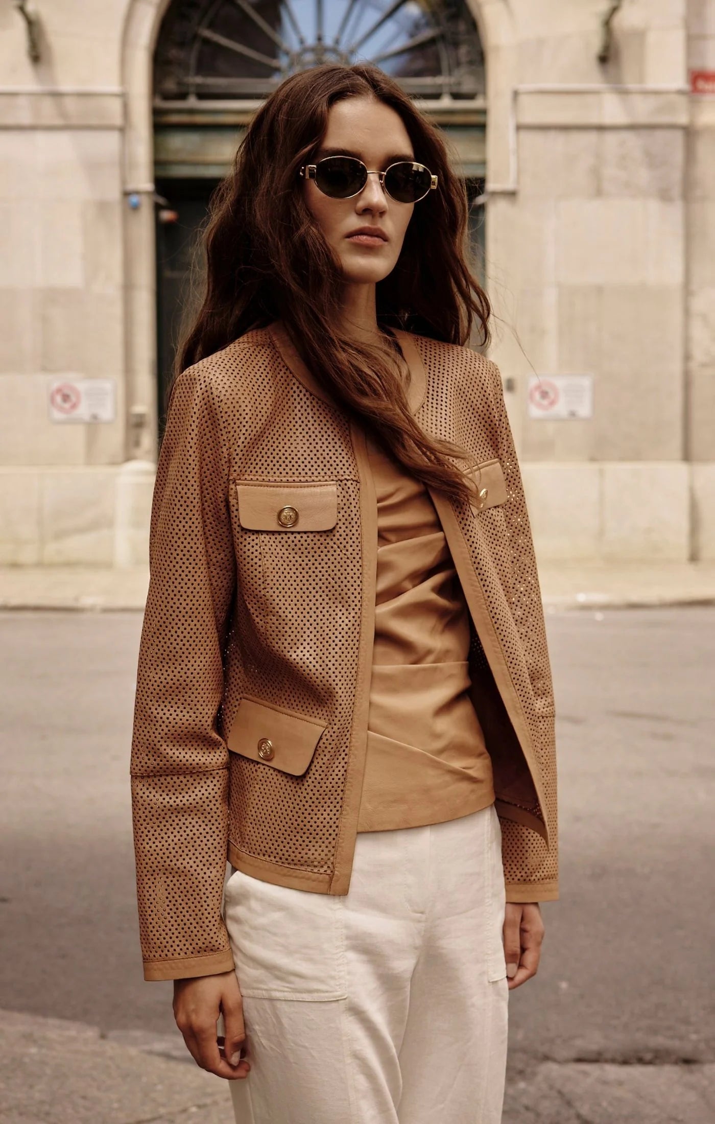 Woman wearing a brown textured leather jacket and sunglasses on a city street.