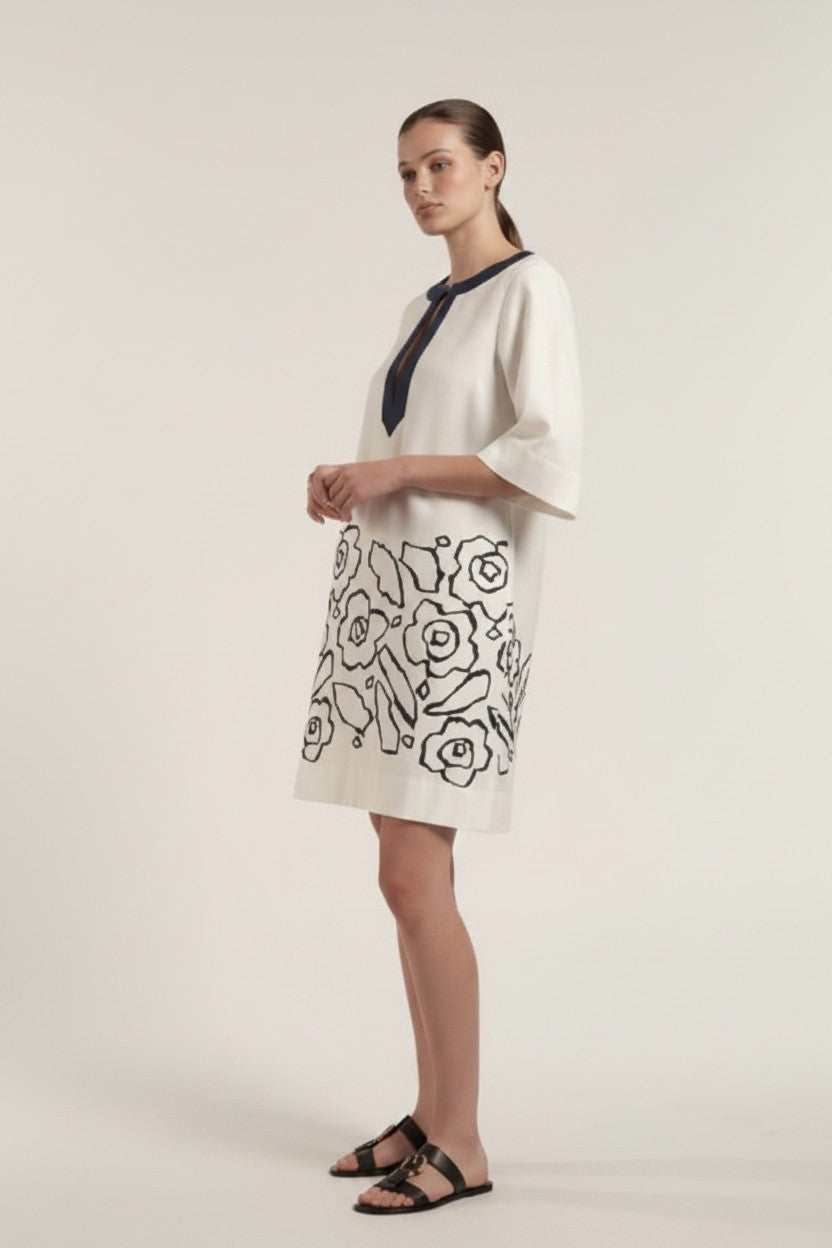 Woman wearing an off-white dress with navy floral patterns on a plain background.