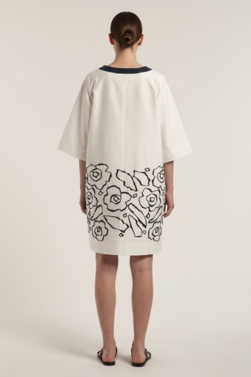 The back of a woman wearing an off-white dress with navy floral patterns on a plain background.