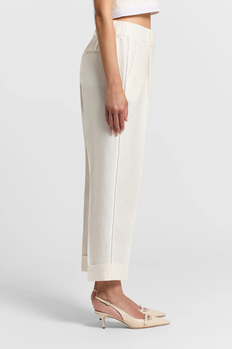 Woman wearing white pants with sparkle side detailing and cream heels on a plain background.