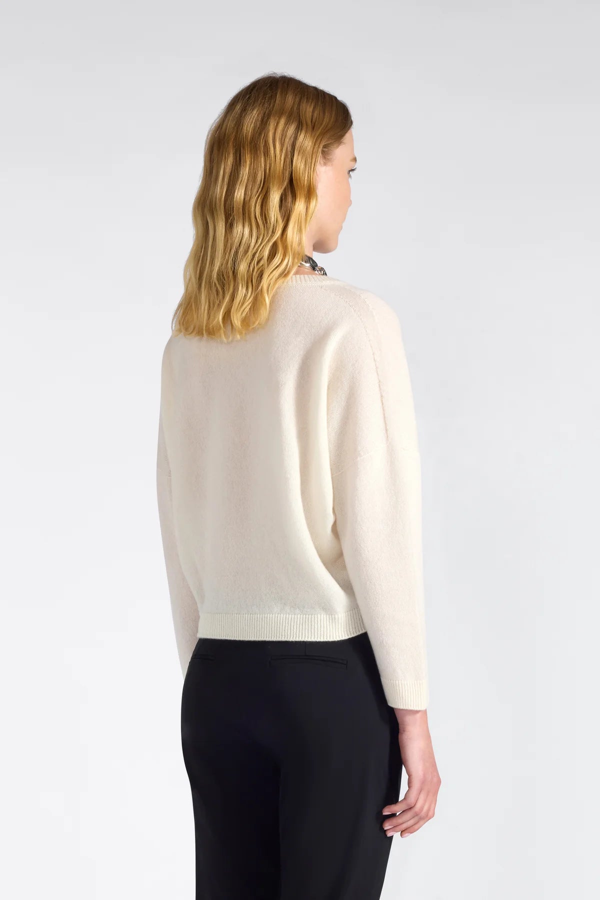 Woman wearing an off white sweater and black pants on a white background.
