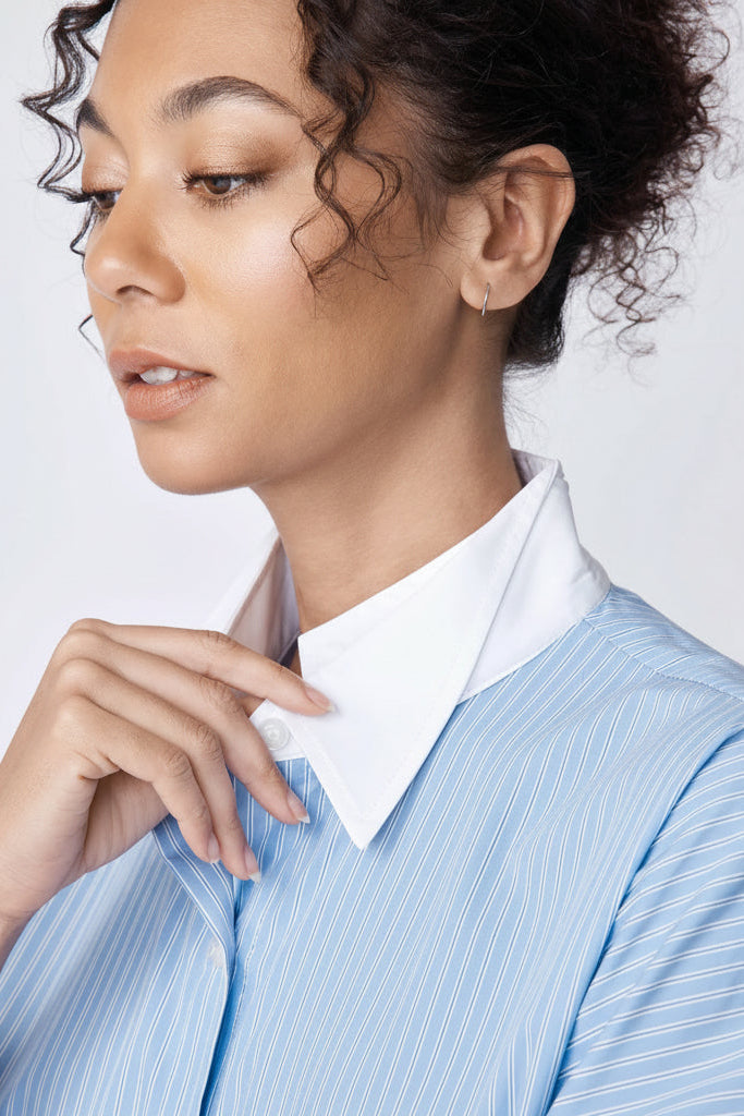 Woman wearing a blue striped shirt with a white collar against a light background