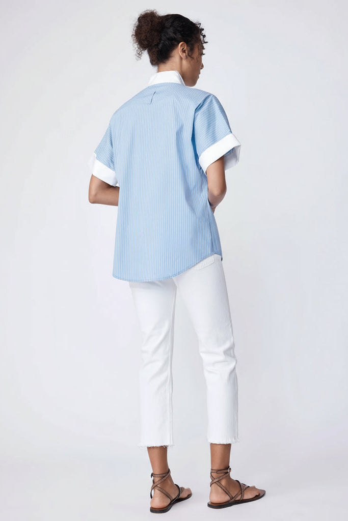 Woman wearing a light blue shirt and white pants on a plain background