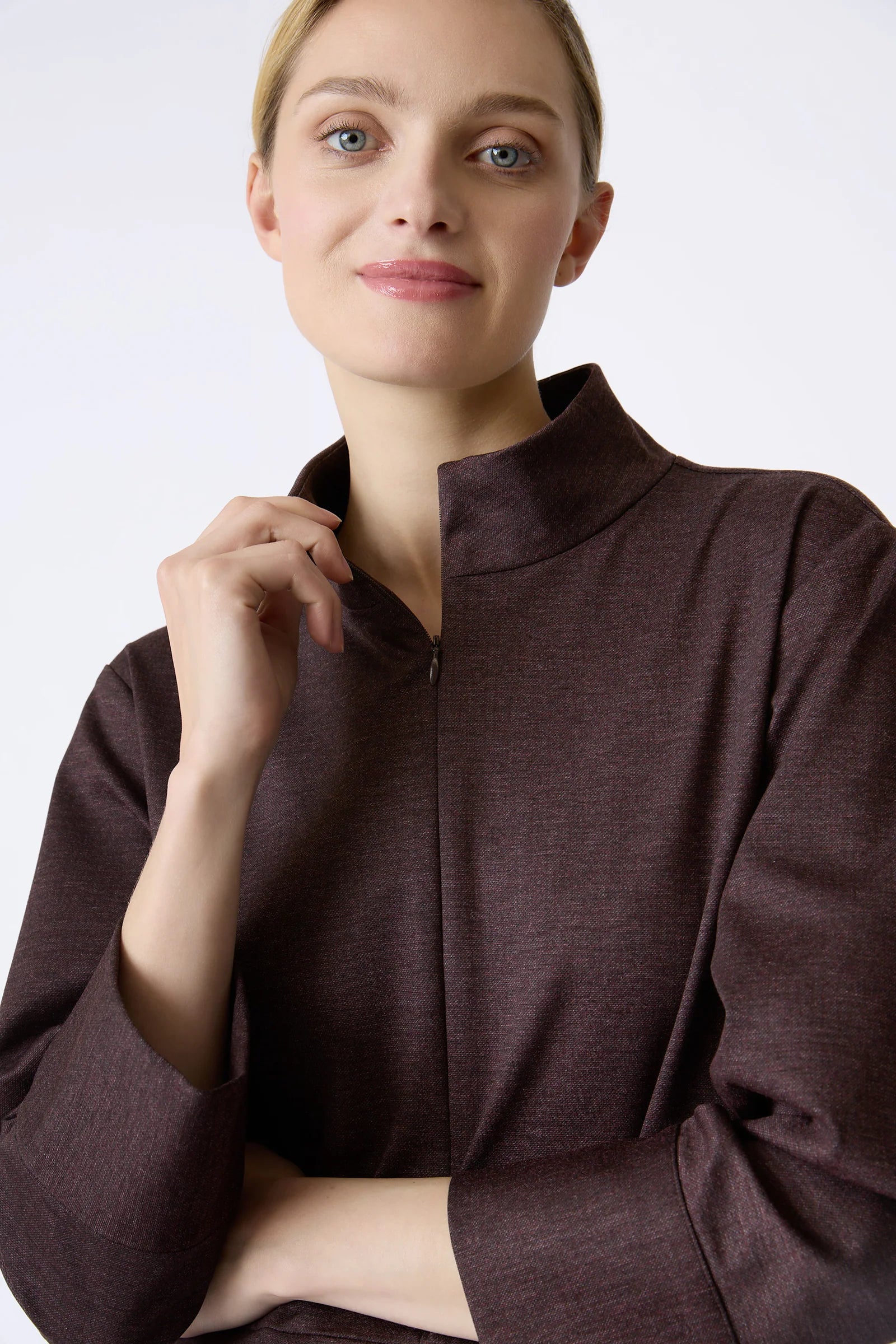 A close-up of a woman wearing a burgundy, long-sleeved dress with a high mock neck and a front zipper, set against a plain light gray background.