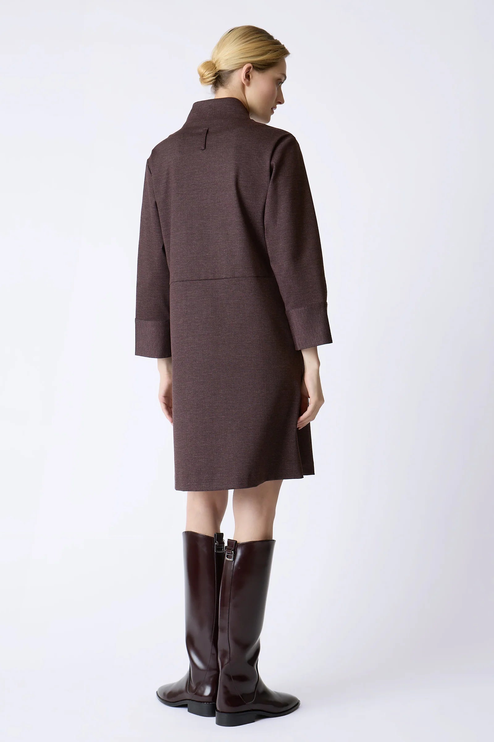 A woman shown from the back wearing a burgundy knee-length dress and matching knee-high boots against a plain light gray studio background.